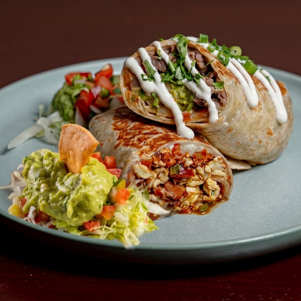 Two burritos, one with steak and guacamole, the other with chicken and bacon, served with salsa and guacamole.