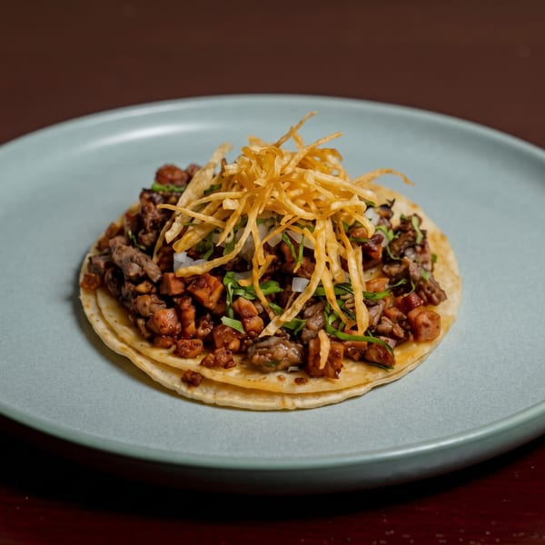 Two tacos with diced meat, onions, cilantro, and crispy fried potato sticks on a light blue plate.